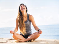 Smiling woman sitting on the beach in a yoga position 