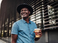 smiling man in hat carrying take out coffee