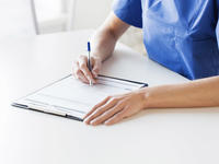 woman in scrubs writing notes on a clipboard